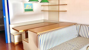 En bäddsoffa som kan göras om till en vanlig soffa, med randigt tyg, ett träbord och två gröna hänglampor.