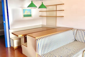 Ein Schlafsofa mit Stoffbezug in Streifenoptik, ein Holztisch und zwei grüne Pendelleuchten.