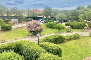 Ein angelegter Garten mit ordentlich geschnittenen Sträuchern, wolkenlosem Himmel und abgestellten Fahrzeugen.