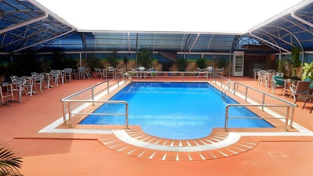 An indoor swimming pool with a glass ceiling, surrounded by chairs and tables. - Mile Stone Hotel & Suites (Lekki)
