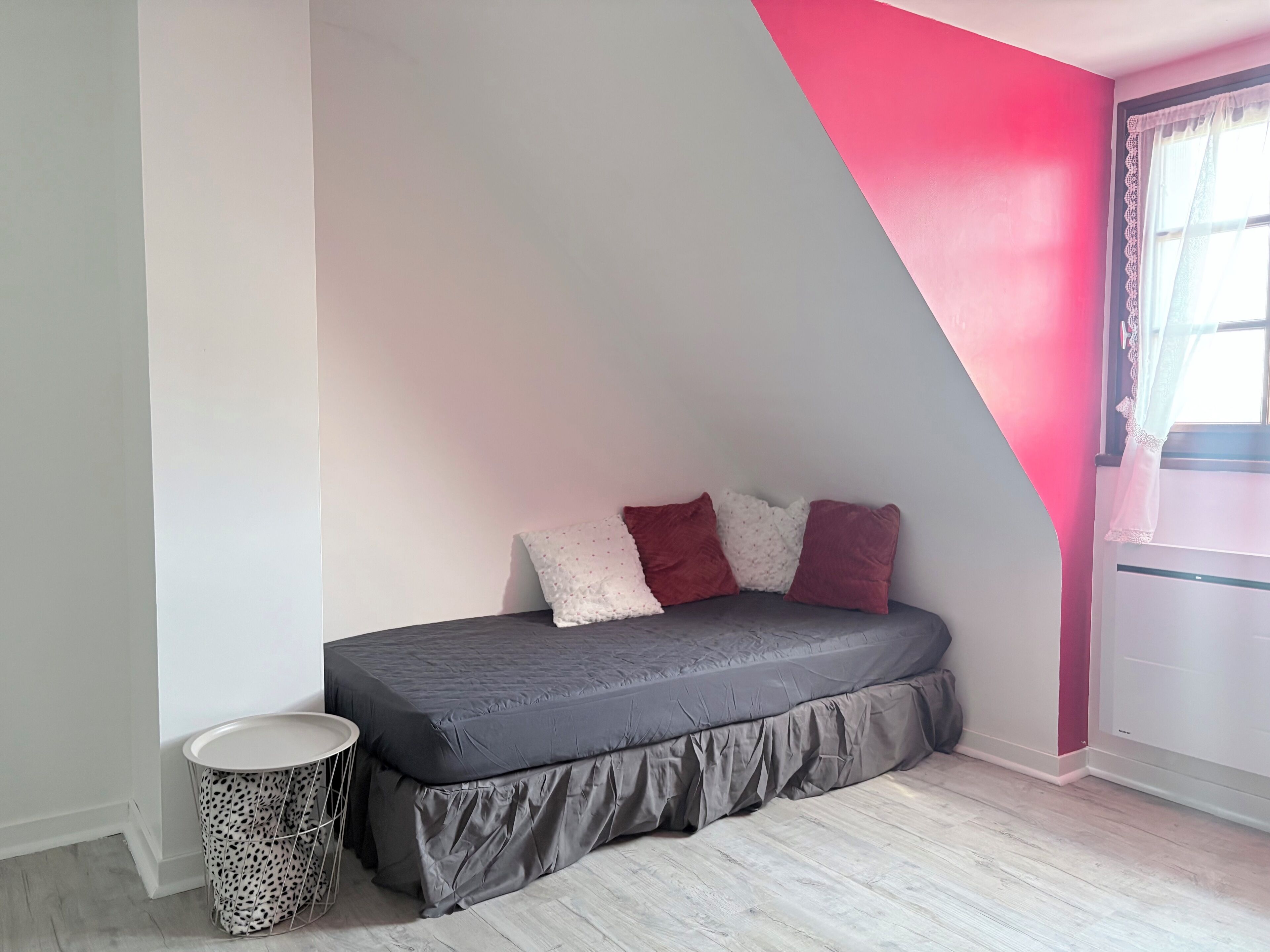 A bedroom with a bed, pillows, a small round table, and a waste basket.