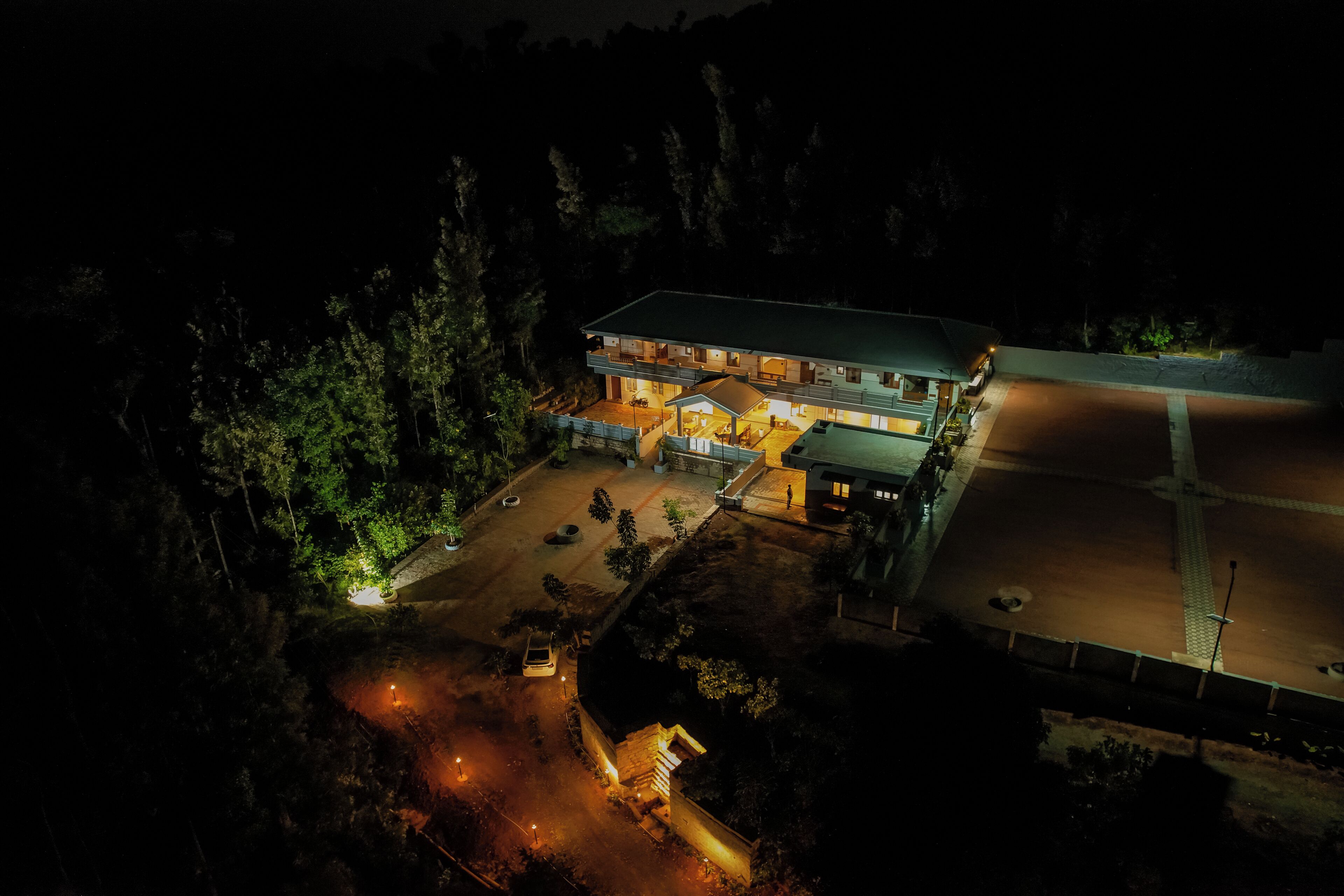 A large building with multiple levels, a parking area, and a surrounding forested area.