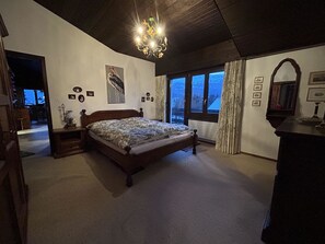 Ein Schlafzimmer mit einem Bett, einer Pendelleuchte, einem Schminktisch und einem Fenster mit Blick.