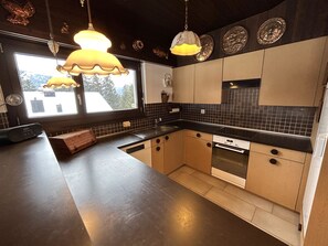 A modern kitchen with a large island, pendant lighting, and a view of the outside.