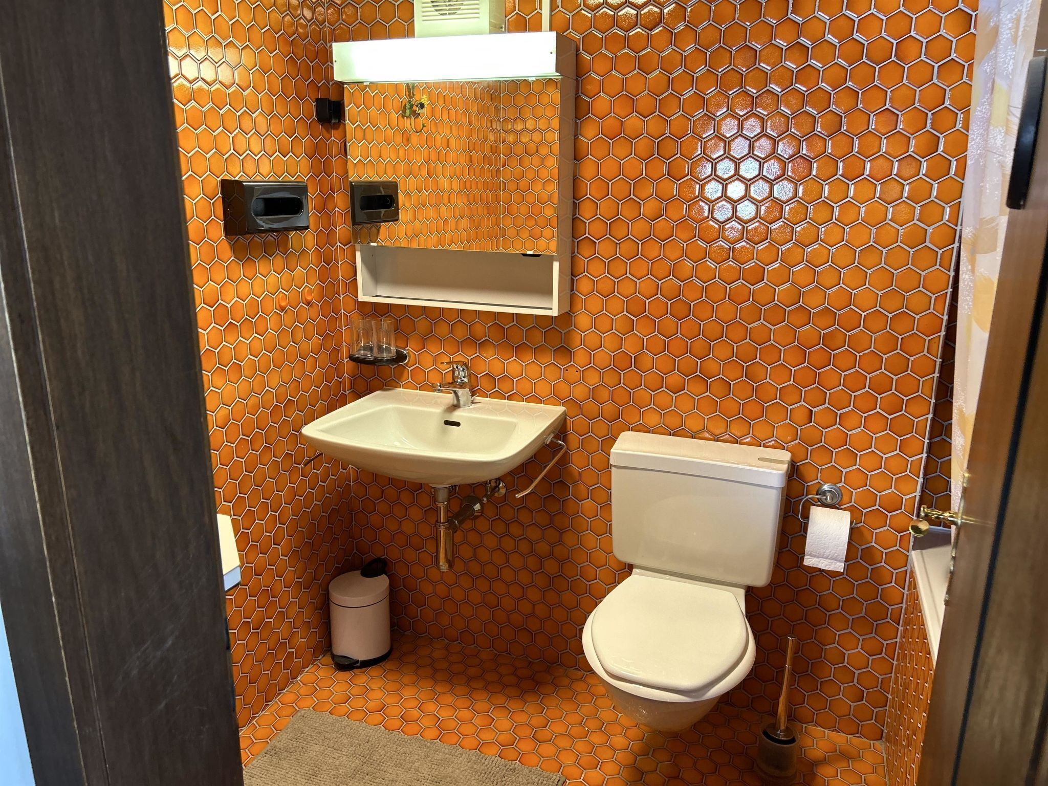 A bathroom with a hexagonal patterned wall, a sink, a toilet, and a trash bin.