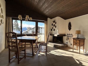 Ein gemütlicher Essbereich mit Holztisch und -stühlen, einem Kamin und Blick auf Berge durch das Fenster.