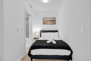 A bedroom with a bed, a nightstand, a lamp, and a painting on the wall. - Midtown Vale Hotel (Toronto)