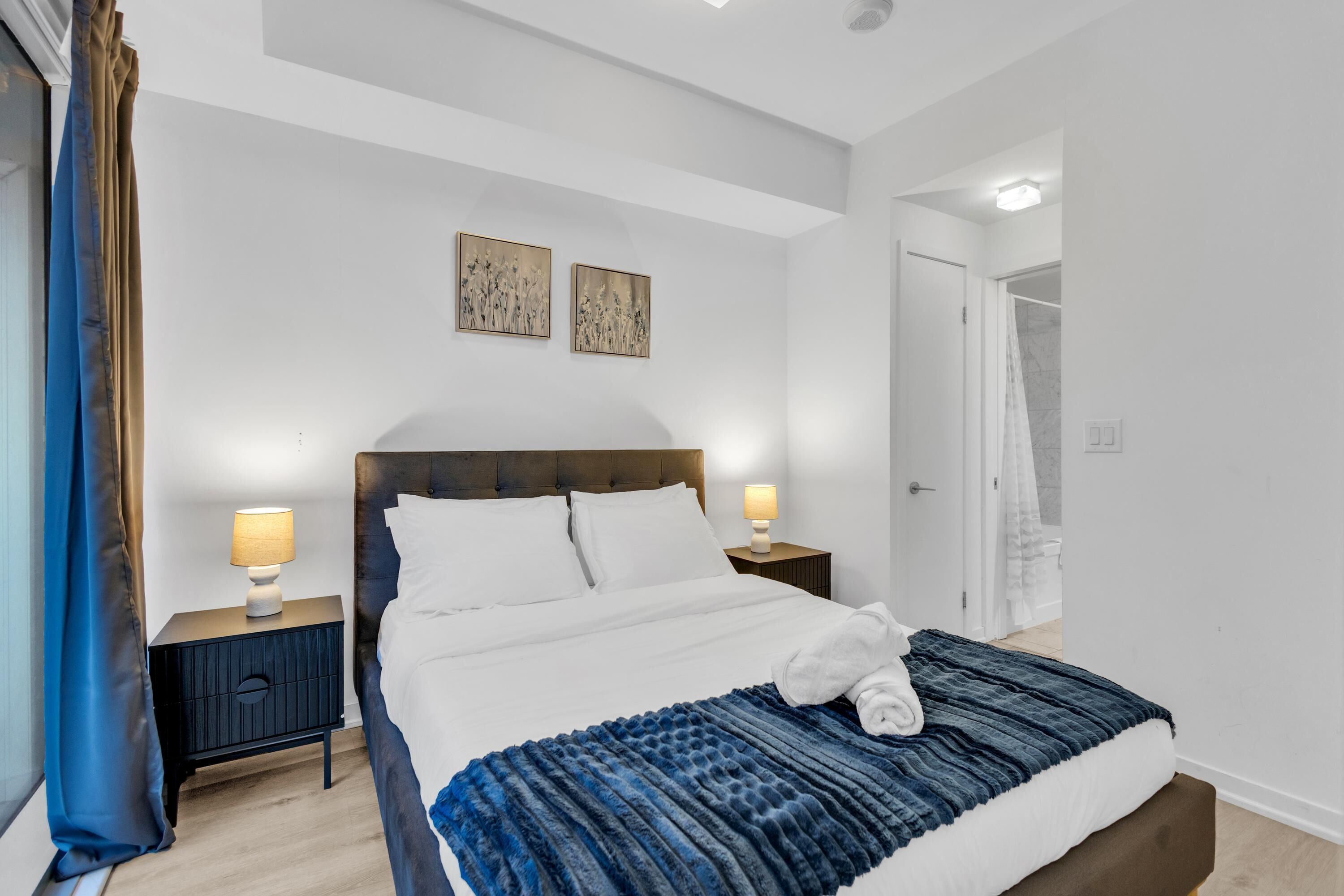 A modern bedroom with a large bed, two bedside tables with lamps, and a door leading to a bathroom.