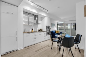 A modern kitchen with white cabinetry, a built-in oven, and a dining area with a round table and black chairs. - Midtown Vale Hotel (Toronto)