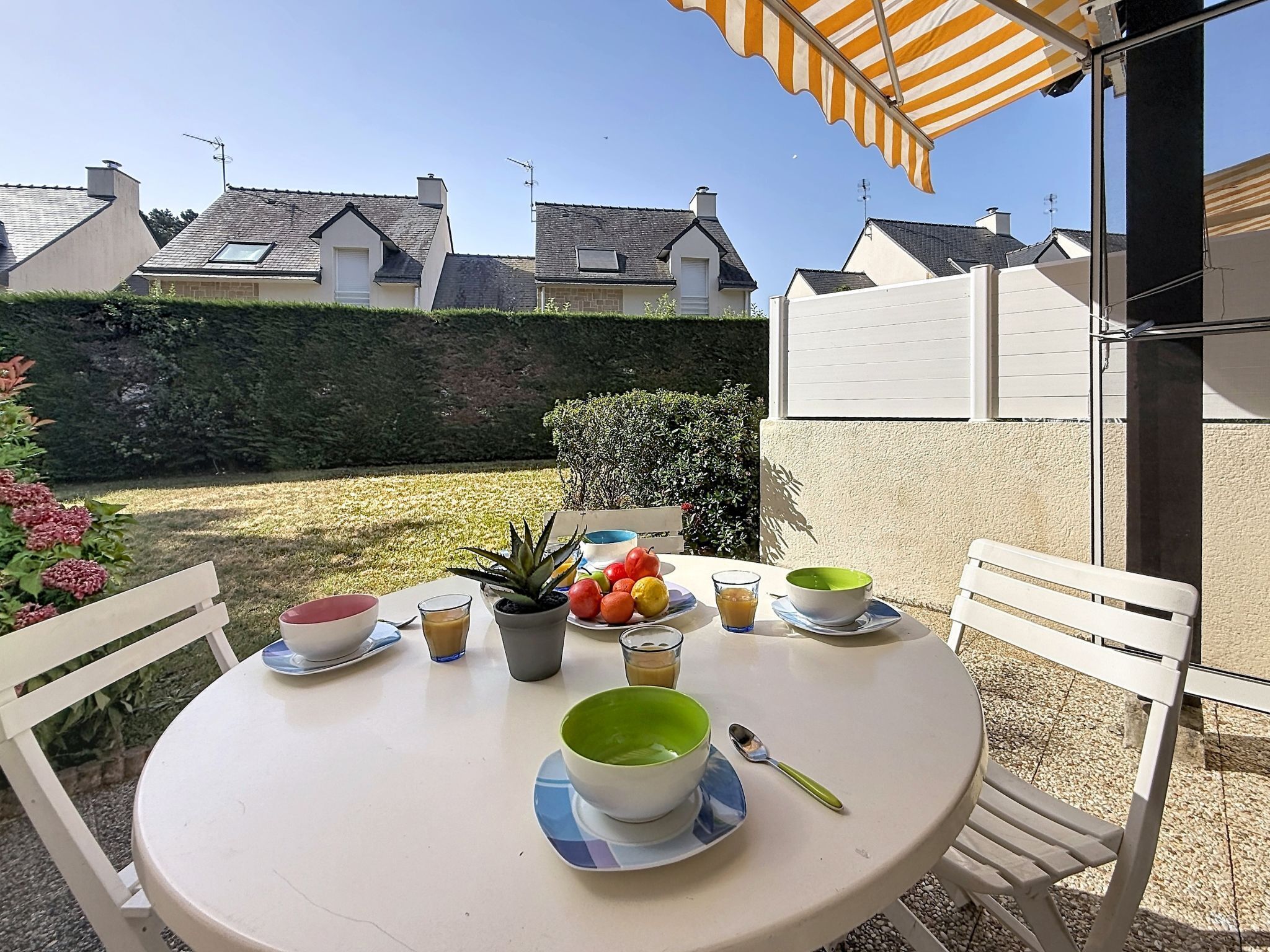 A round table with a white tablecloth, surrounded by white chairs, under a striped awning.