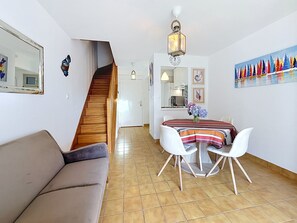 Een woonkamer met een bank, een eettafel met stoelen, een trap en een keuken op de achtergrond.
