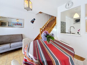 A dining area with a striped tablecloth, a wooden staircase, a sofa, and a wall clock. - Salicornia by Interhome (Carnac)