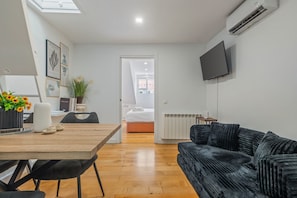 Ein modernes Wohnzimmer mit einem Holzesstisch, einem schwarzen Polstersofa und einem flachbildfernseher an der Wand.