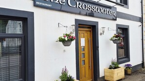 Un edificio con un letrero que dice 'The Crosswater Restaurant' y 'PUB'. Hay macetas de madera con flores en la entrada.