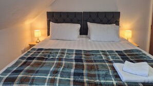 Una cama con una colcha escocesa, dos almohadas blancas y dos lámparas de noche.