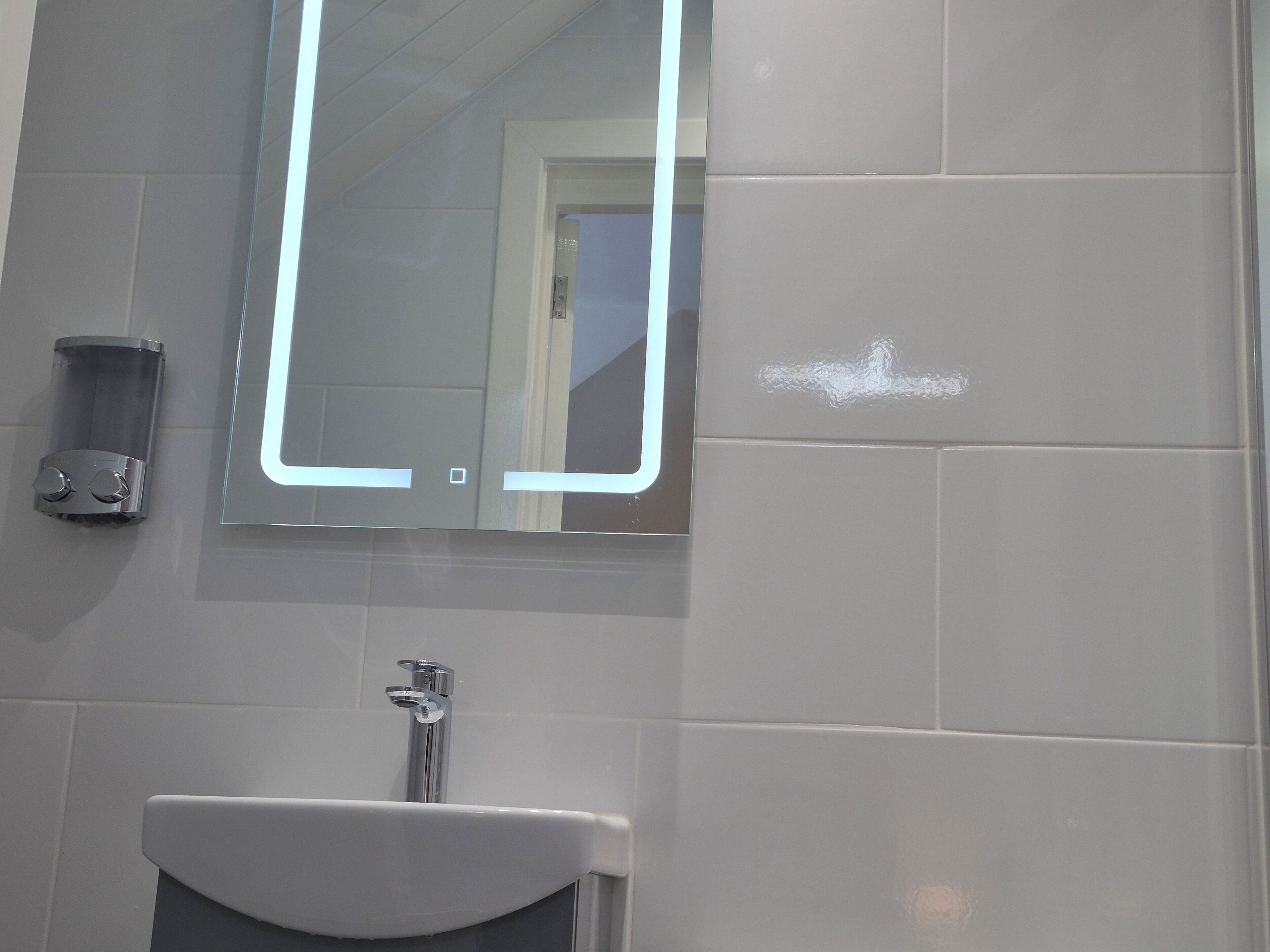 Un baño con lavamanos blanco, espejo y dispensador de jabón.