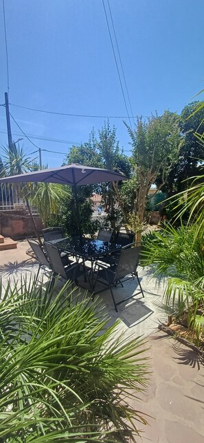 Ein Außenbereich mit Tisch und Stühlen, umgeben von Grünflächen und blauem Himmel.