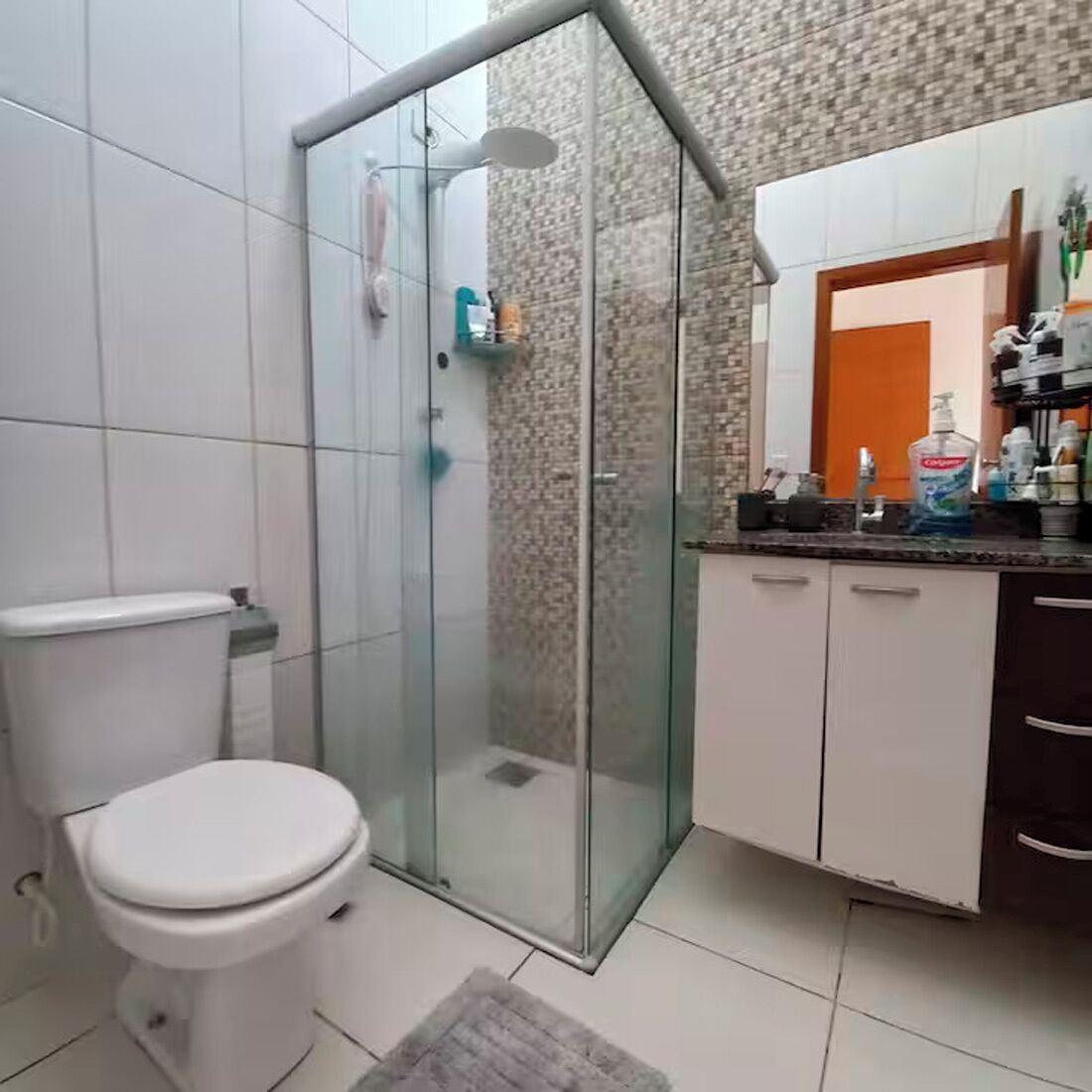 Un baño con inodoro, cabina de ducha de vidrio y tocador con espejo.