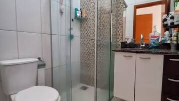 Un baño con inodoro, cabina de ducha de vidrio y tocador con espejo.