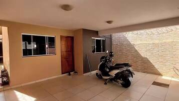 A spacious room with tiled flooring, a wooden door, a window, and a scooter parked inside.