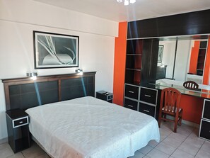 Ein Schlafzimmer mit einem Bett, einem Nachttisch, einer Kommode, einem Sessel und einem Spiegel.