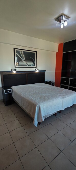 Ein Schlafzimmer mit Bett, Nachttisch, Kommode, einem gerahmten Bild an der Wand und einer Deckenleuchte.