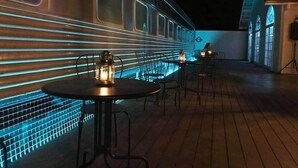 Un train aux éclairages bleus, des tables décorées de bougies et un bâtiment aux fenêtres en arc de cercle.