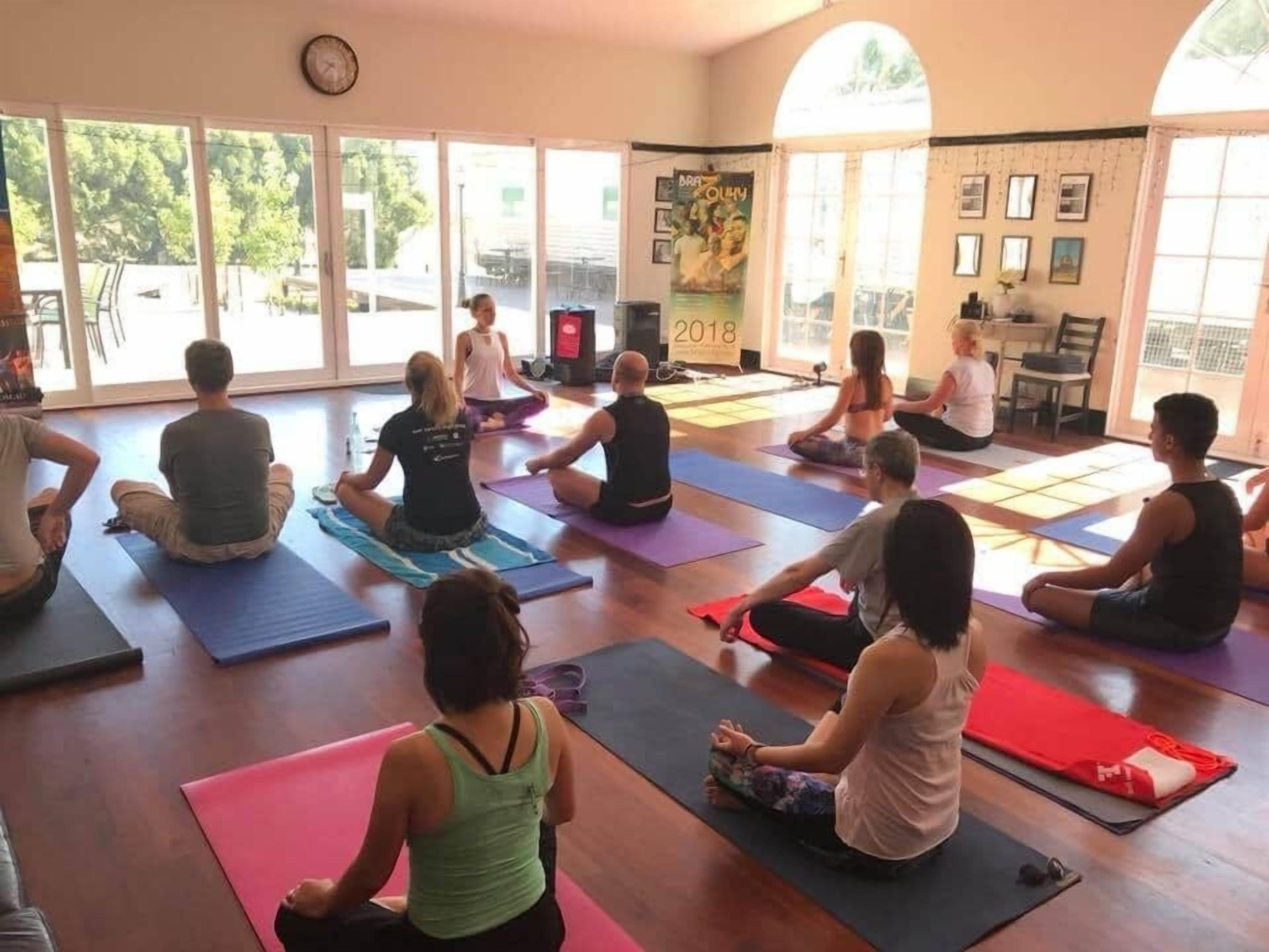 A yoga class in a room with large windows, a clock on the wall, and a poster.