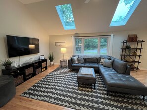 Un salon comprenant un téléviseur, un canapé, un pouf et un tapis à motifs.