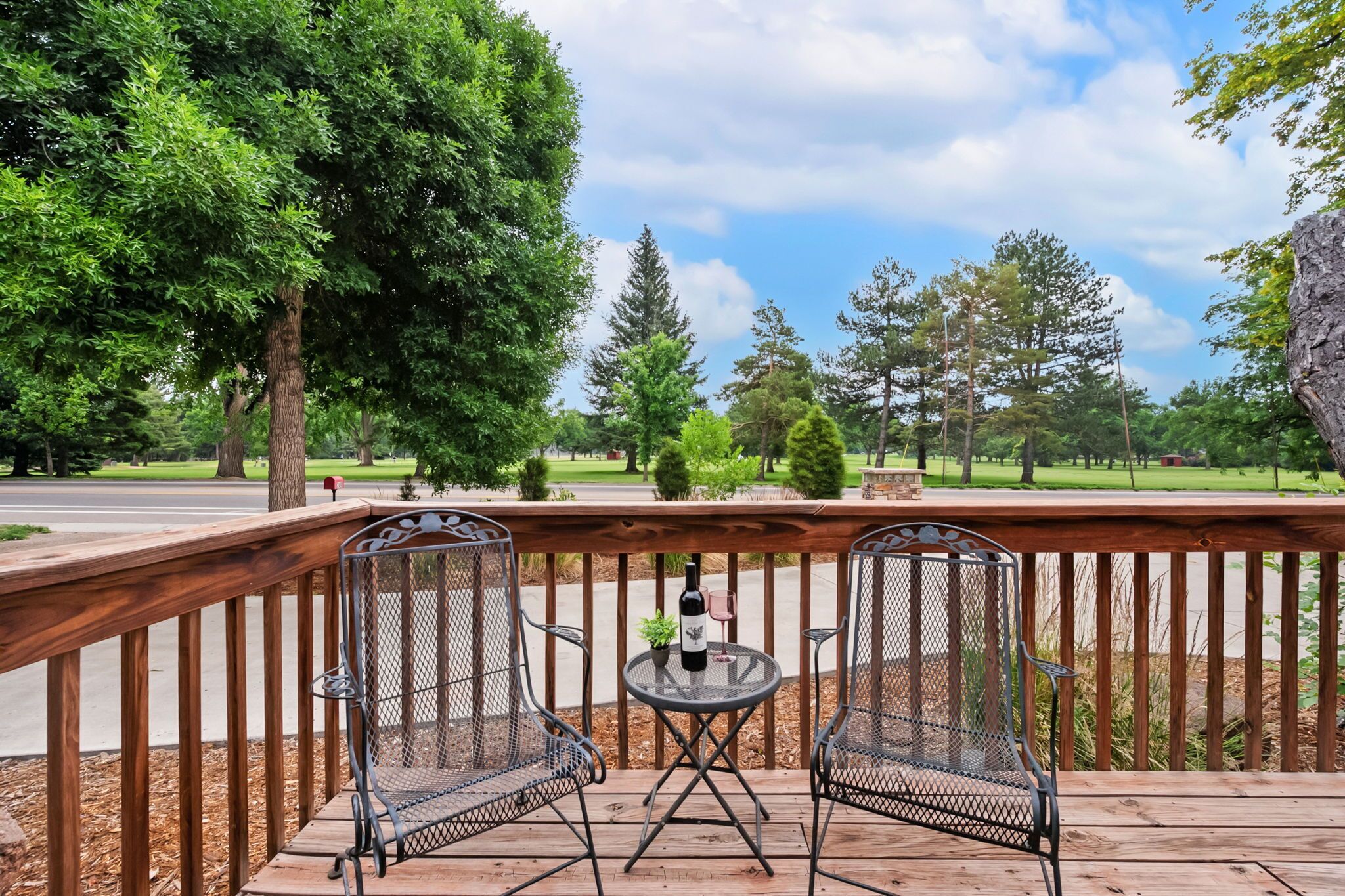 A deck with two metal chairs and a small table, a bottle, and a glass.