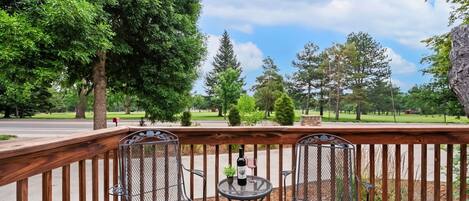 A deck with two metal chairs and a small table, a bottle, and a glass.