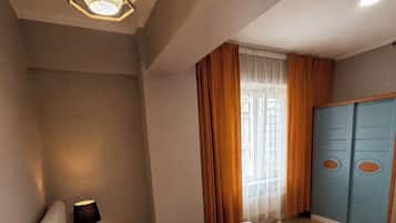 Habitación de hotel con cama, mesita de noche, lámpara, armario y ventana con cortinas.