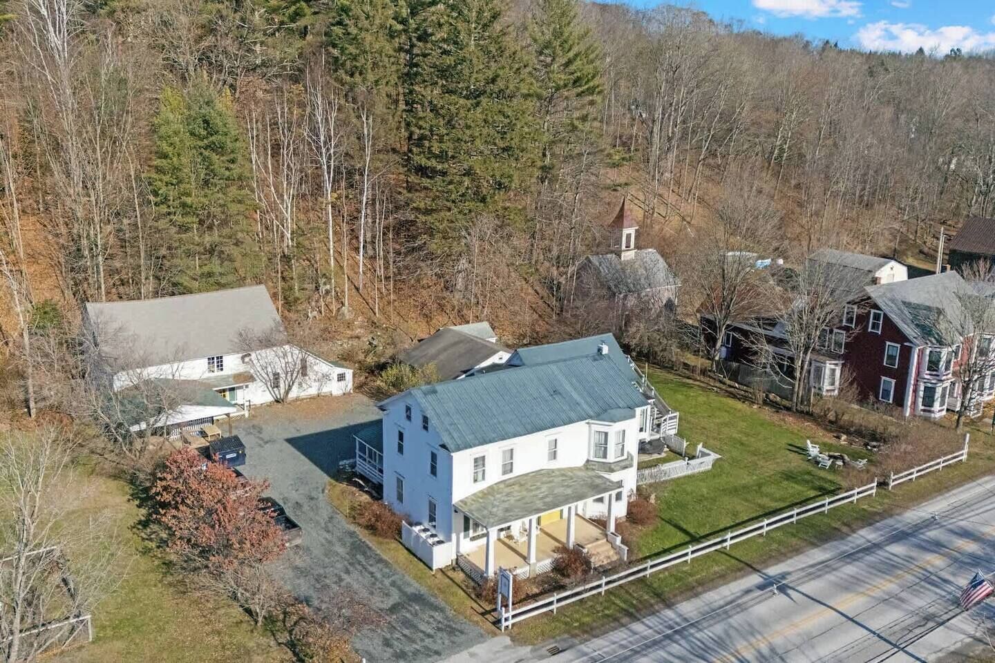 A large white house with a green roof, surrounded by trees and a road.