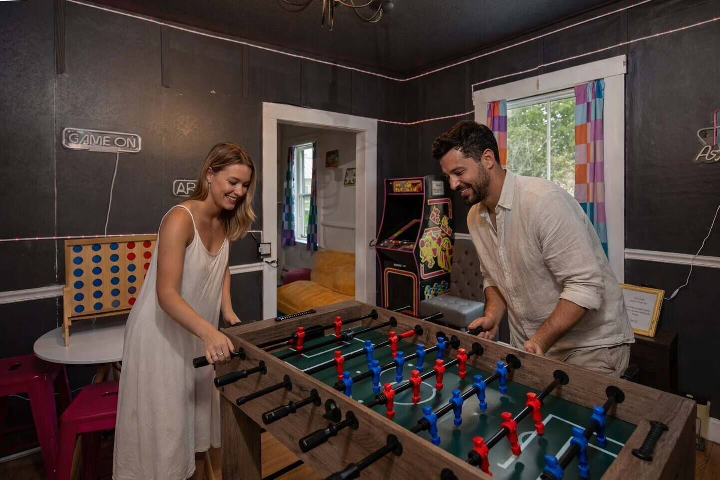 A room with a foosball table, a dartboard, and a small table with a chair.