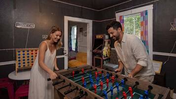 A room with a foosball table, a dartboard, and a small table with a chair.