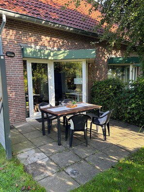 Un patio con una mesa y sillas, un muro de ladrillo y un toldo verde.