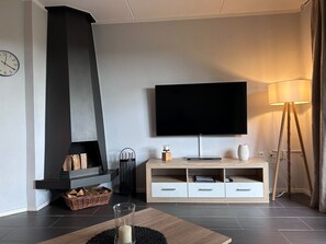 Una sala moderna con chimenea, un televisor de pantalla plana montado en la pared, una mesa de centro de madera y una lámpara de pie.