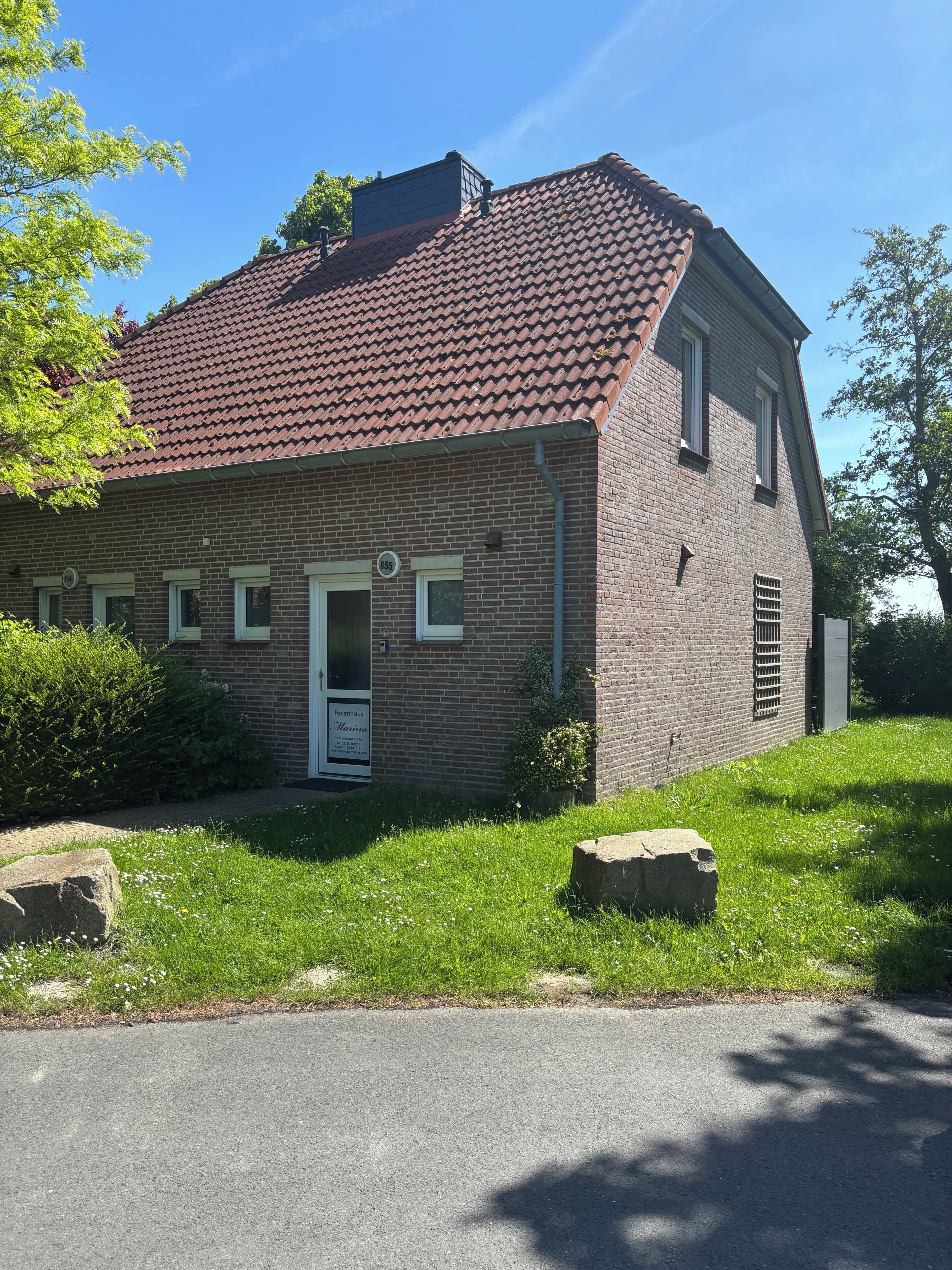 Ein Backsteinhaus mit rotem Ziegeldach, einer weißen Tür und einem kleinen Garten mit Steinen und Rasen.