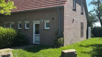 Ein Backsteinhaus mit rotem Ziegeldach, einer weißen Tür und einem kleinen Garten mit Steinen und Rasen.