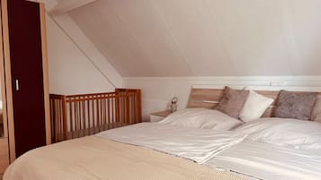 Ein Schlafzimmer mit schrägen Wänden, einem Holz-Kinderbett, einem Nachttisch mit einer Laterne und einem Bett mit weißer Bettwäsche.