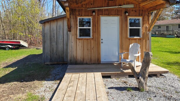 Une cabane en bois avec une porte, deux fenêtres, une terrasse et une chaise.
