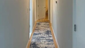 A hallway with a patterned carpet, a ceiling light fixture, and a door at the end. - Grammy’s Cape Cod Summer House (Brewster)