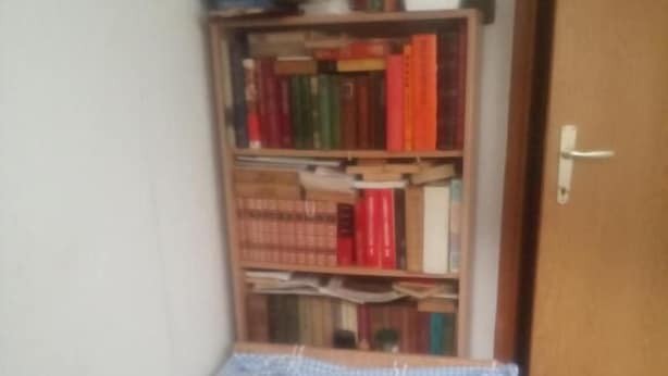 A small room with a single bed, a bookshelf, and a door.