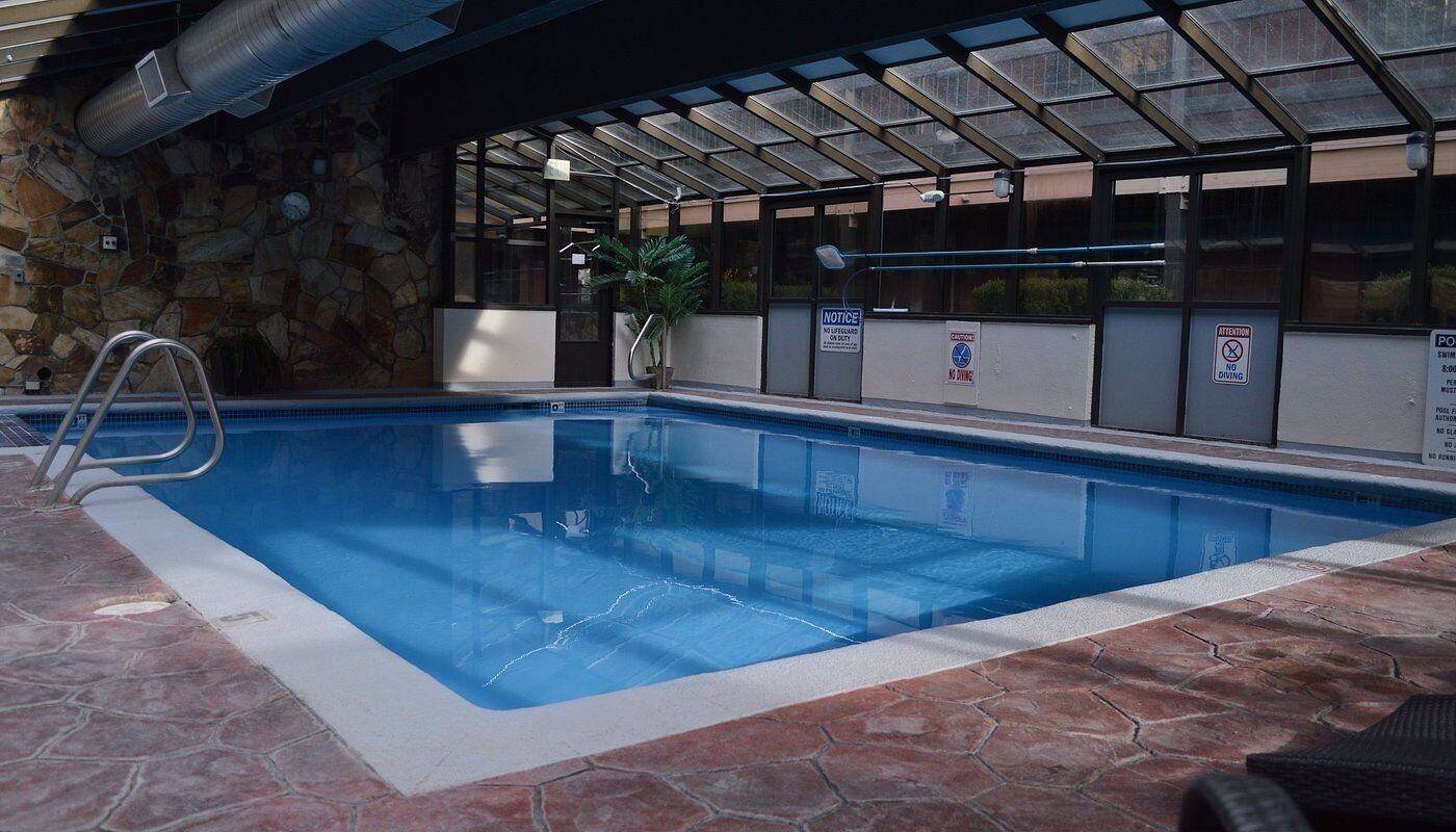 Una piscina interior con pared de piedra, una escalera metálica y señales de seguridad.