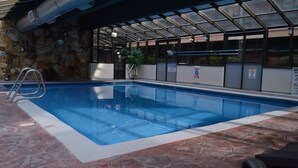 En indendørs swimmingpool med stenvæg, metalstige og sikkerhedsskilte.