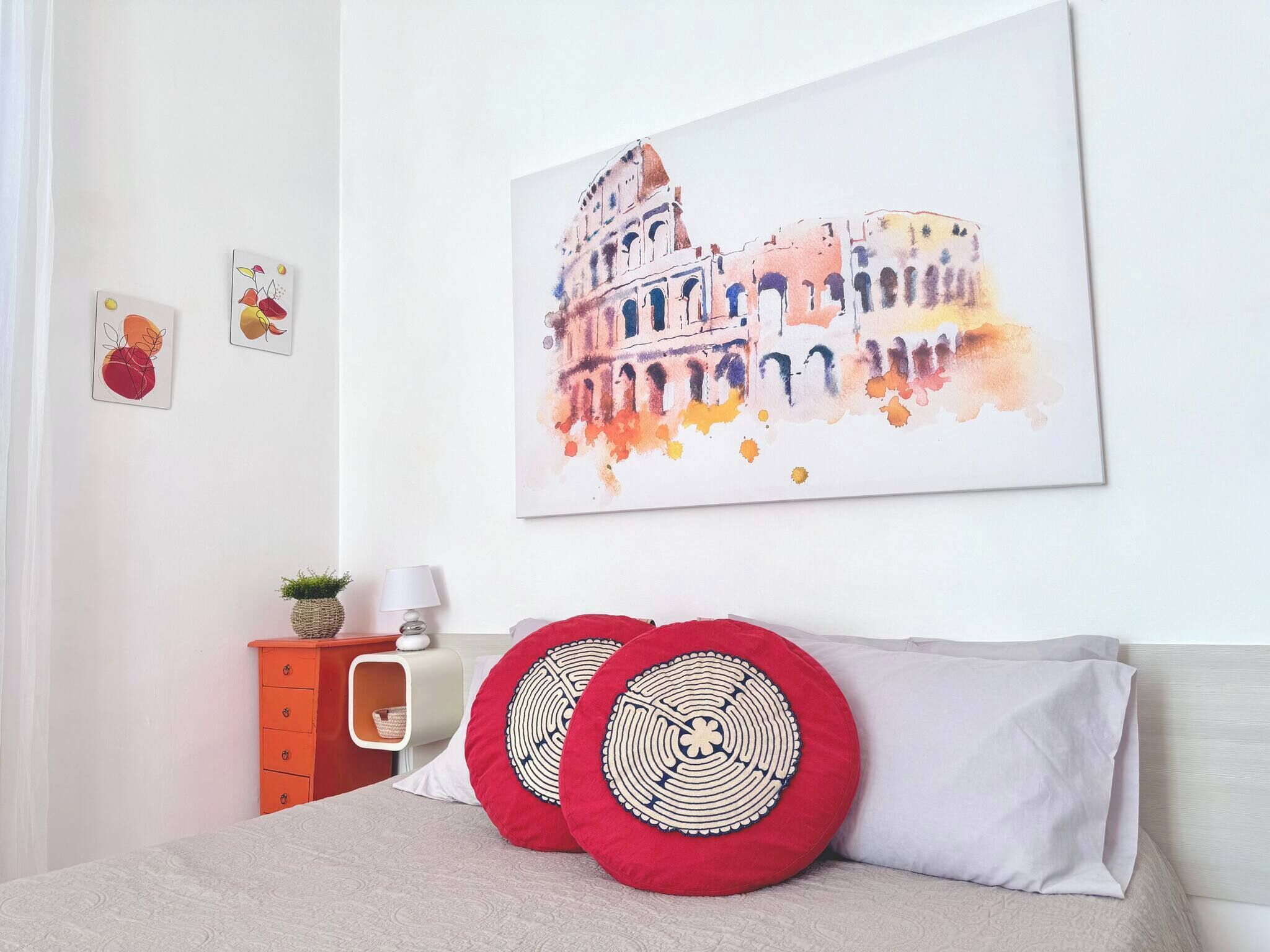 A bedroom with a bed, pillows, a nightstand, a lamp, and a wall painting.