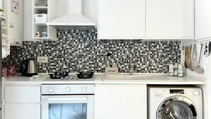 A compact kitchen with a microwave, oven, and washing machine, white cabinets, and a tiled backsplash. - Central Rome Apartment Termini - Roman Haven (Rome)