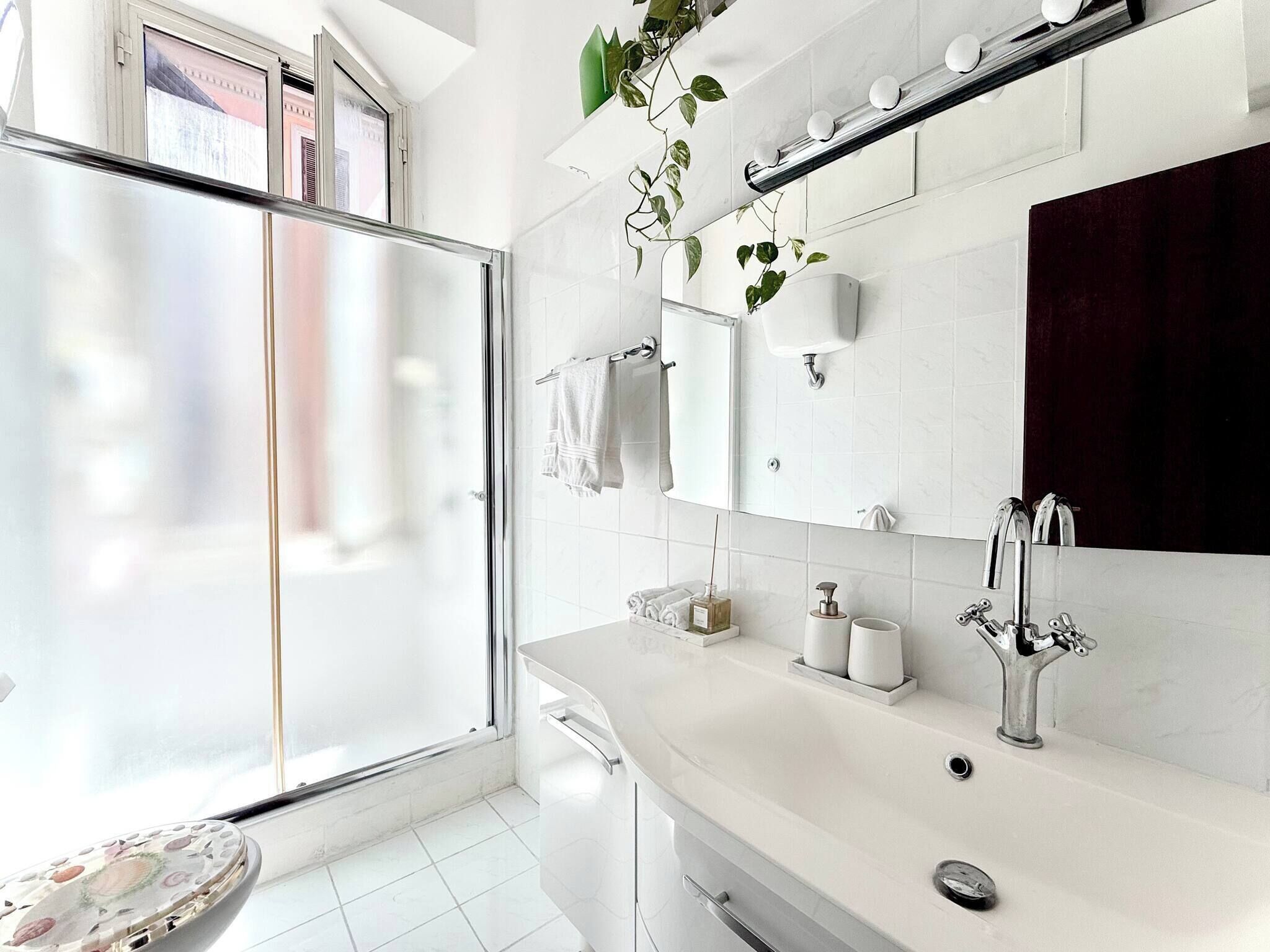 Een moderne badkamer met een glazen douchecabine, een witte wastafel met spiegel en een potplant.