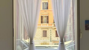 A window with sheer curtains, a view of a building with a balcony, and a sign that reads 'HOTEL' on the building facade.