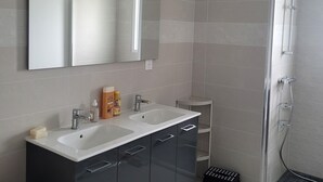 A modern bathroom with a double sink vanity, a large mirror, a shower enclosure, and a small stool. - Spacious single-story house (Villeneuve-en-Retz)